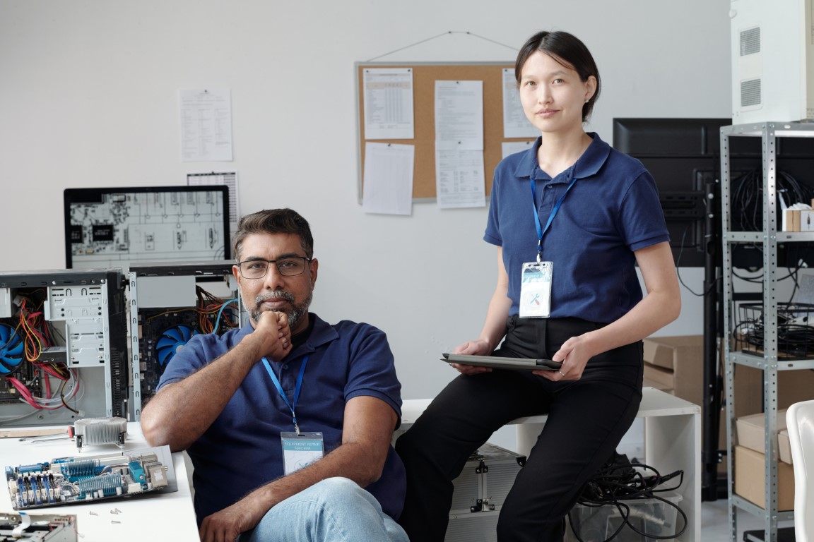 Portrait of IT professionals engaged in tech tasks in a laboratory environment, surrounded by computer equipment and network devices, both wearing identification badges looking at camera